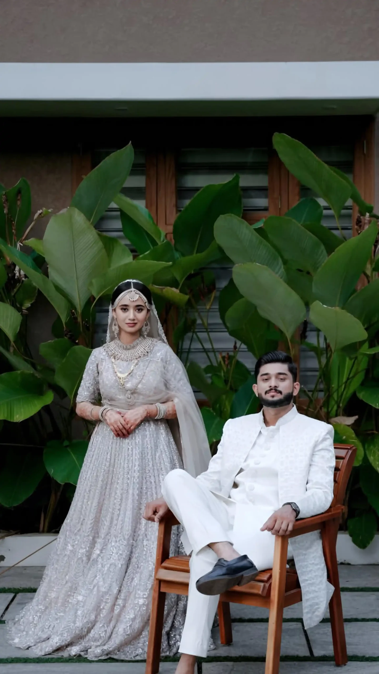 Bride in white dress standing beside groom seated on a chair, captured by the best wedding photographer in Malappuram.